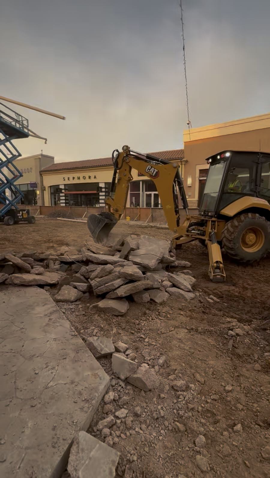 Backhoe breaking up a concrete slab at a shopping center site