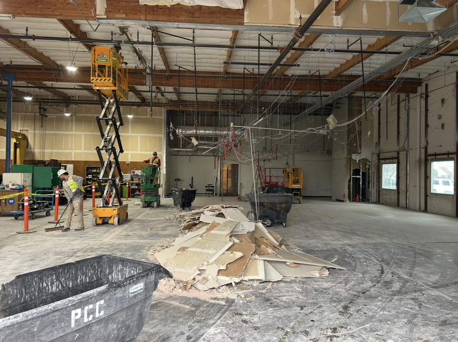 Pile of drywall debris with workers and lifts in a large interior
