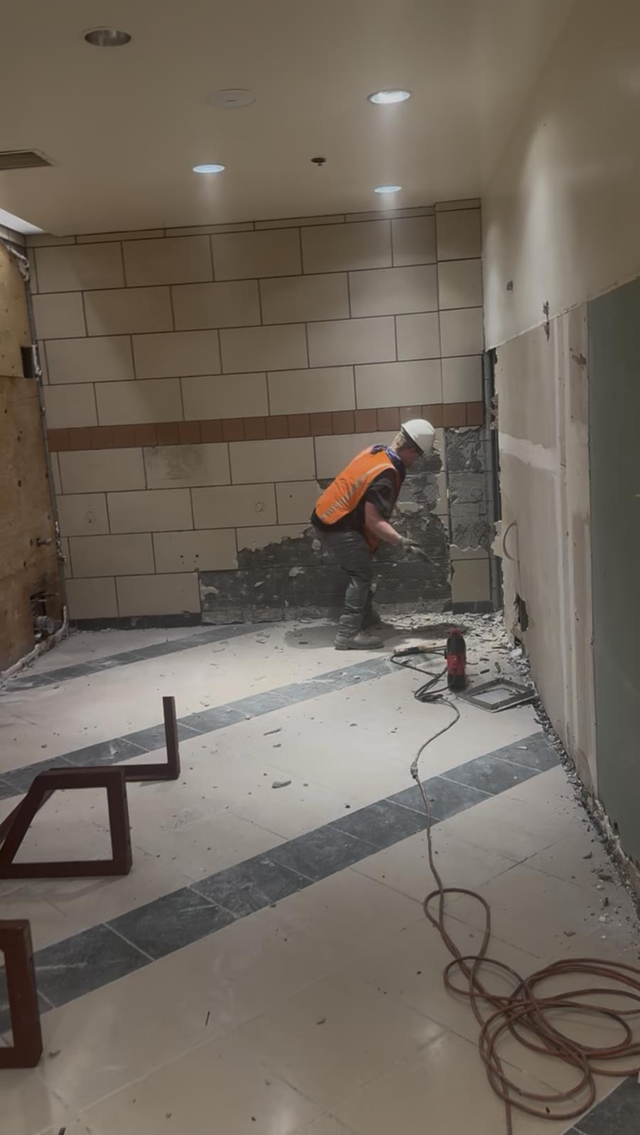 Worker removing wall tile with hand tools